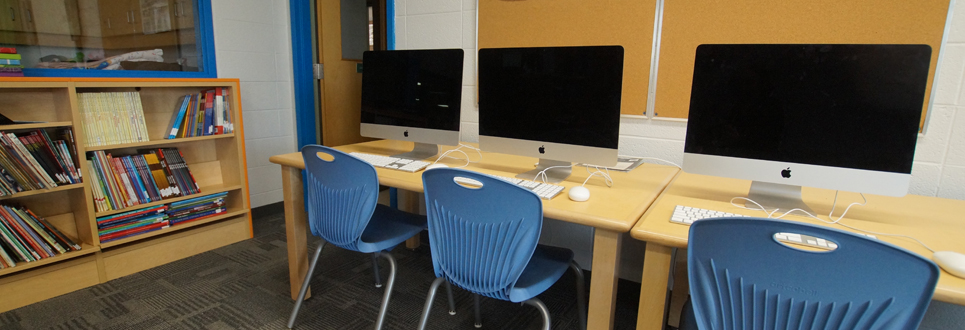 Three Apple Computers sitting on a table with chairs